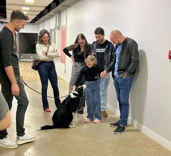 Cinco adultos ao lado de uma criança passando a mão em um cachorro.