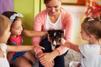 Professora com cachorro no colo e alunos fazendo carinho