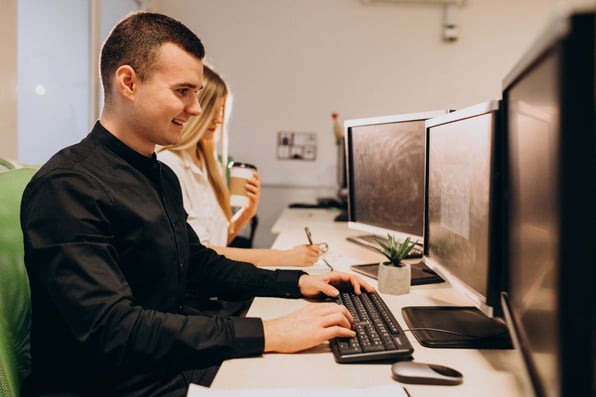 Homem escrevendo no teclado do computador ao lado de uma mulher