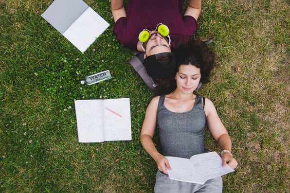 Homem e mulher deitados no gramando estudando.