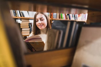 Mulher lendo um livro no corredor de uma biblioteca.