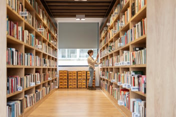 Mulher pegando um livro em uma prateleira de uma biblioteca.