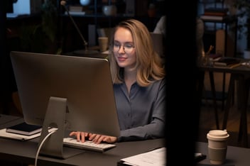 Mulher de óculos digitando em seu computador.