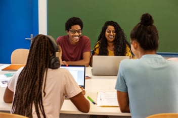 Grupo de estudantes reunidos a mesa, rindo e conversando.