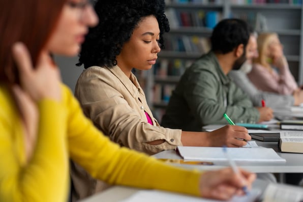 Grupo de pessoas sentadas em classes, escrevendo em papéis.