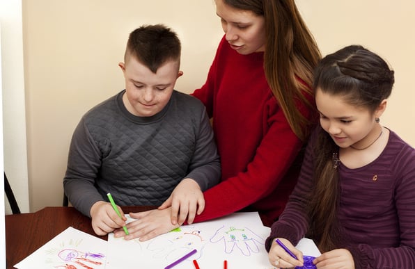 Duas crianças com deficiência sendo auxiliados por professora.