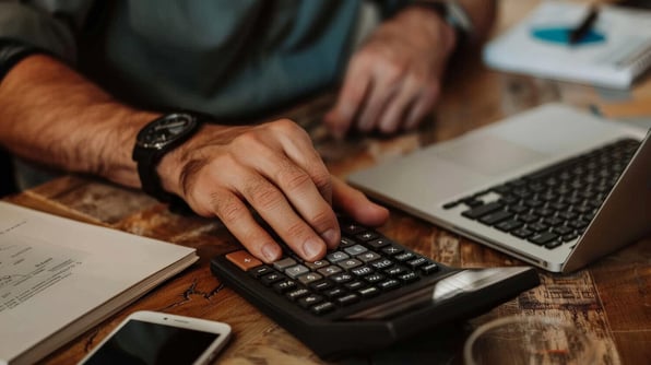 Homem utilizando calculadora em frente ao notebook.