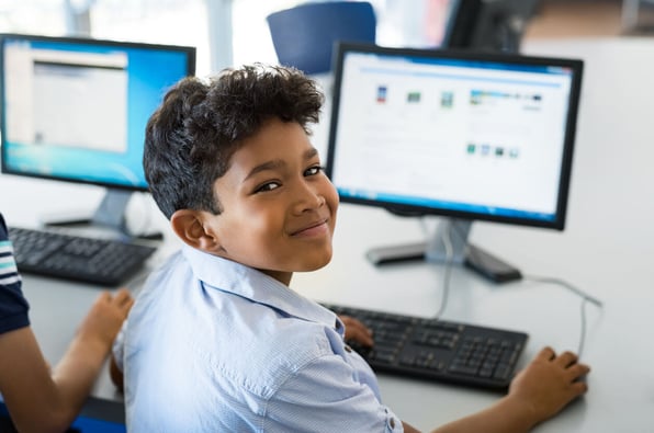 Menino em frente a um computador sorrindo para a câmera