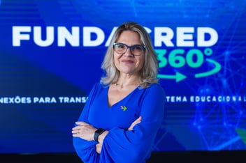 mulher loira, vestida de blusa azul, centralizada em frente à telão de LED com escrito Fundacred Ventures 360 graus