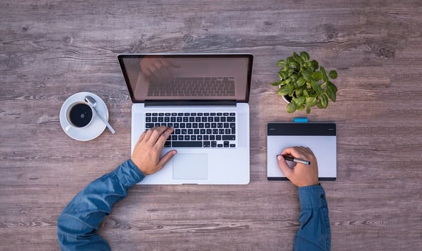 Homem usando um bloco de notas, um notbook e tomando um café