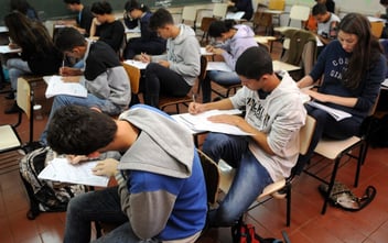 Alunos em sala de aula estudando com livros e cadernos.