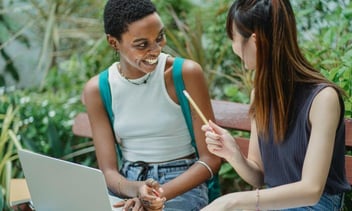 Duas jovens sentadas e conversando, enquanto estudam.