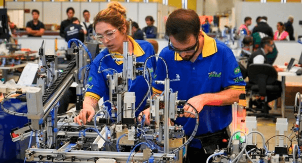 Dois jovens, uma mulher e um homem, mexendo em uma máquina.