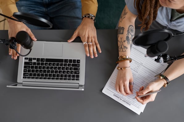 Pessoas a mesa, com notebook e bloco de folhas. Ângulo de cima.