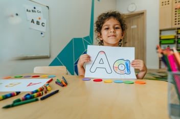 Menina segurando caderno com a letra 