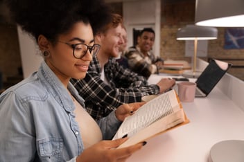 Jovem mulher lendo livro em sala de aula.