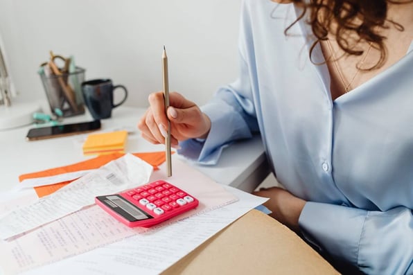 Pessoa sentada em uma mesa e mexendo em uma calculadora. 