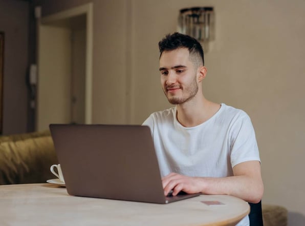 Homem sentado mexendo em um notebook em cima de uma mesa. 