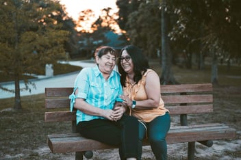 Duas idosas sentadas em um banco e sorrindo. 