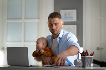 Homem trabalhado em seu notebook com seu filho no colo.