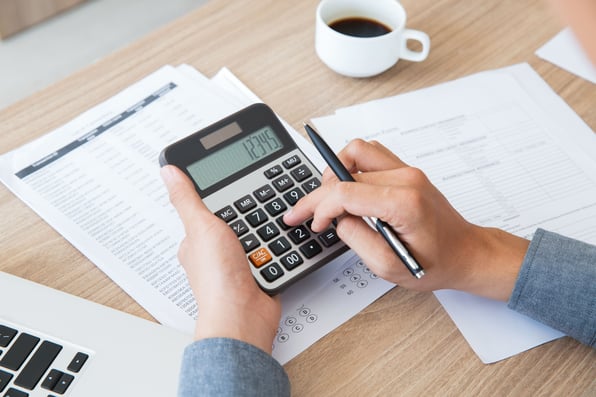 Uma pessoa digitando em uma calculadora em frente a papéis.