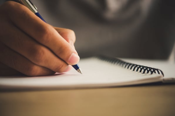 Mão segurando uma caneta e escrevendo em caderno.