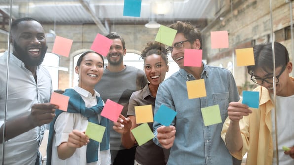 Grupo de pessoas interagindo em frente ao vidro com post-its.