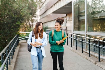 Duas garotas andando e sorrindo com livros em mãos