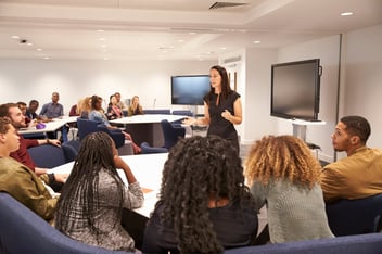 Professora ensinando para um grupo de alunos em sala de aula.