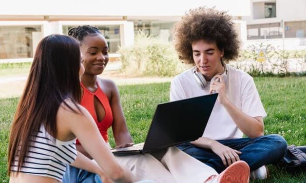 Três jovens sentados na grama, com notebook.