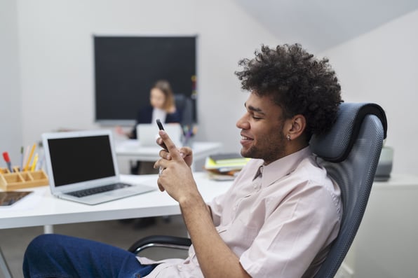 Homem sentado a mesa mexendo em um celular em suas mãos.