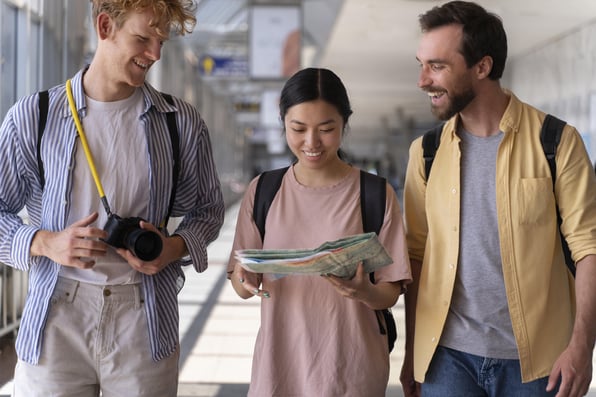 Três jovens, um do lado do outro, com um mapa na mão e mochila nas costas.