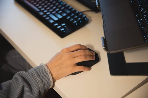 Mão segurando um mouse ao lado de um teclado.