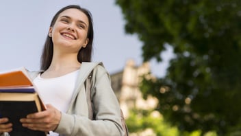 Estudante sorrindo e segurando livros em um campus universitário.