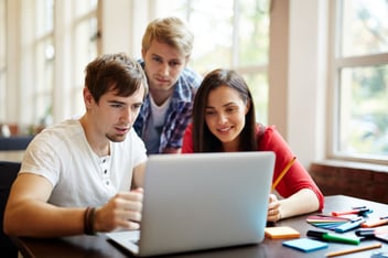 Três jovens sorrindo enquanto olham para tela de notebook.