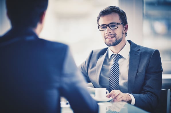 Dois homens de terno, sentados a mesa, conversando.